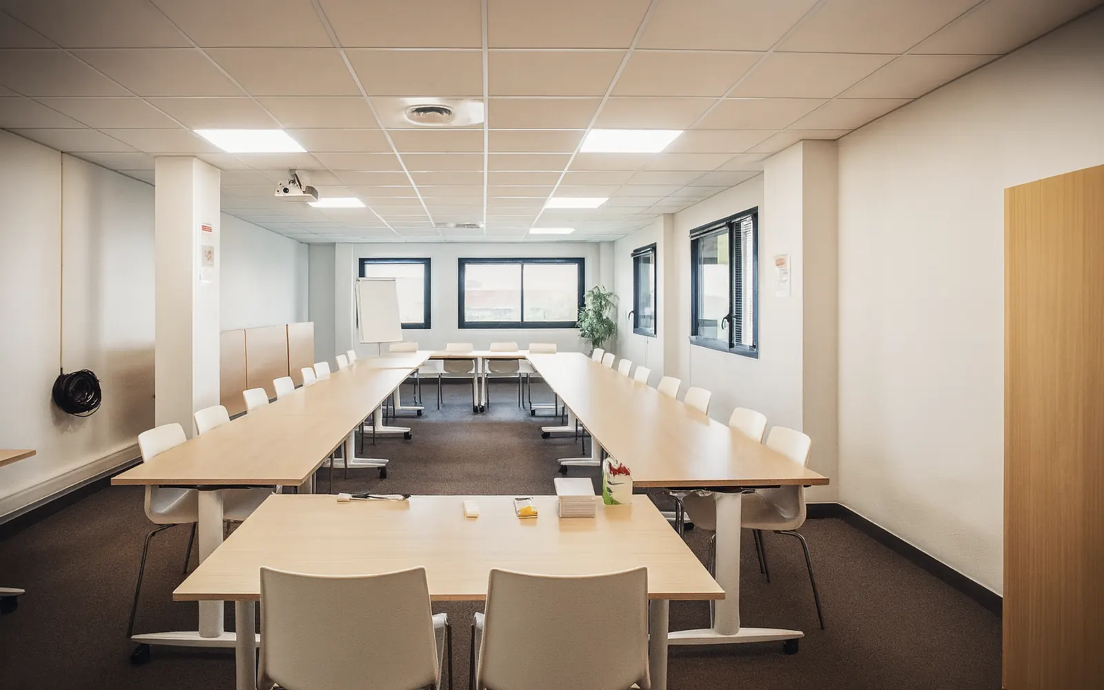 Salle de réunion connectée Solea à Espace Entreprise Garosud, Montpellier : tables en U face à l'écran de projection, prête pour une réunion hybride